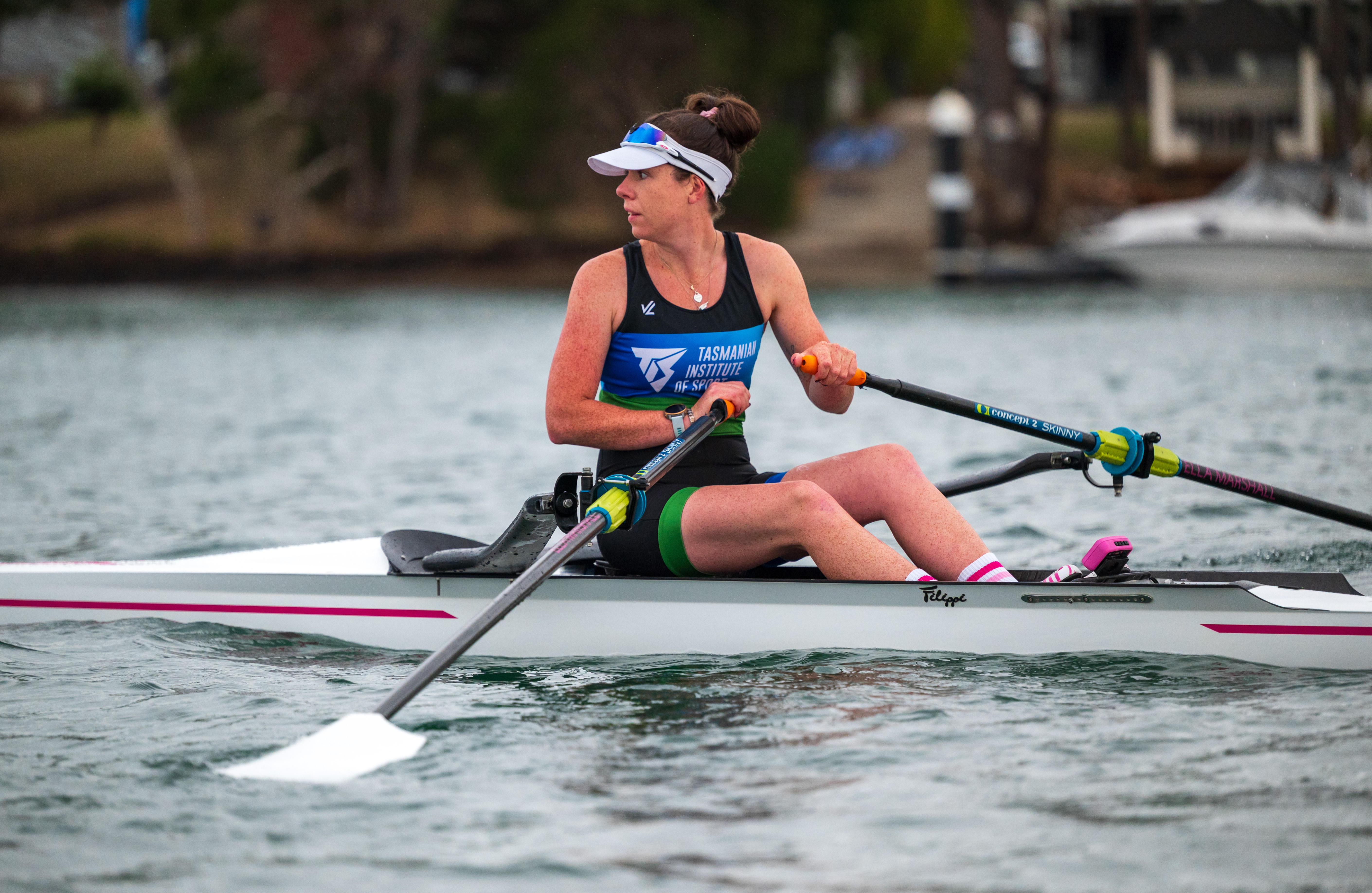 Ella is in a single rowing shell on the water at Lake Barrington, looking back over her shouler